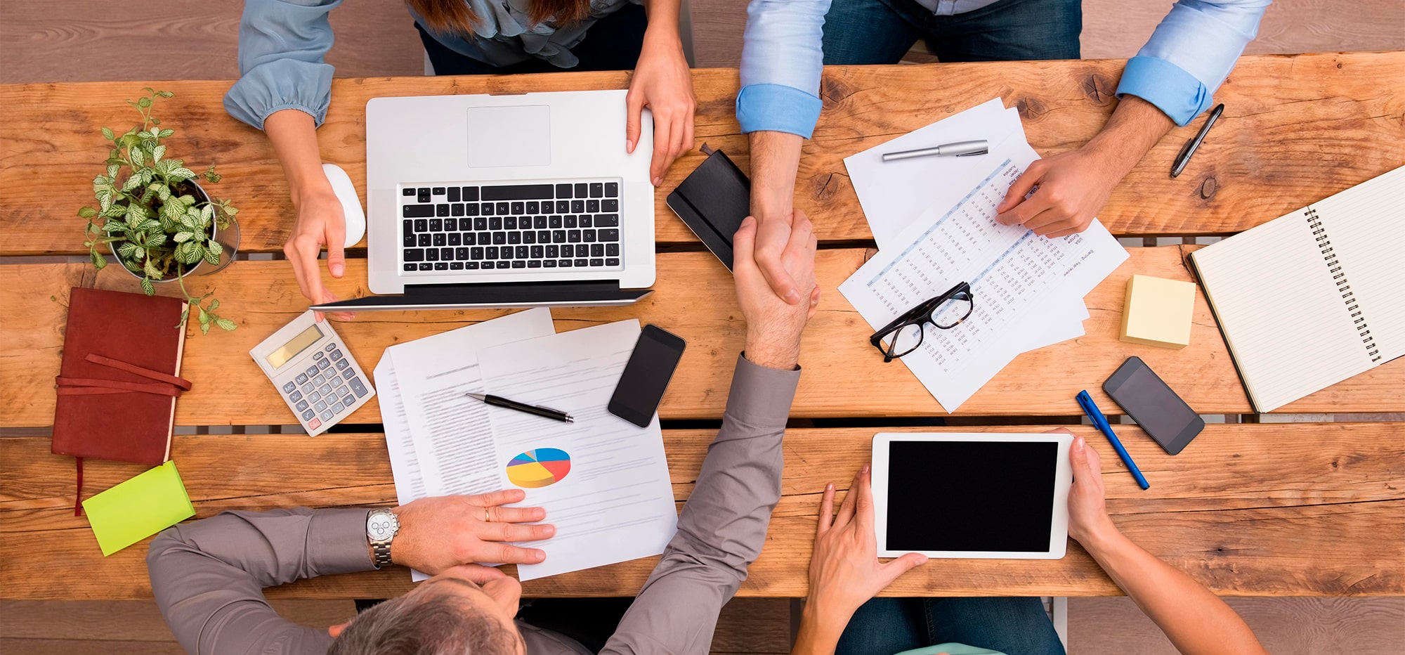 Vista panorámica de un equipo de trabajo planificando, sentados en una mesa dándose la mano.